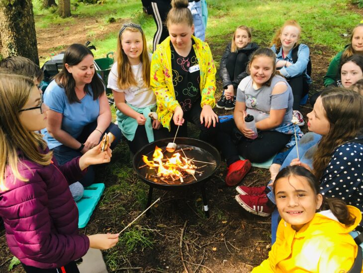 Group of girls sitting round campfire toasting marshmallows